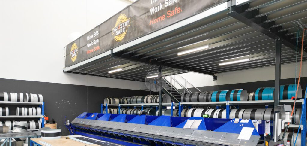 Industrial mezzanine storage platform above metal coil racks, maximising warehouse space and efficiency.